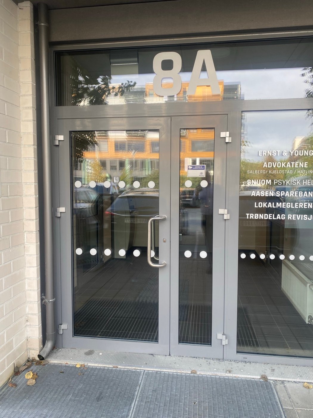 Inngangen med glassdører. På vinduet står navnene på firmaene i bygget, blant dem Snuom Psykisk Helse.